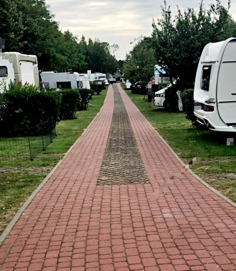 Miejsce kempingowe. Po obu stronach chodnika biegnącego wzdłuż fotografii - przyczepy kempingowe