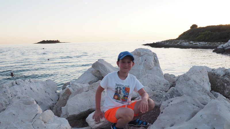 Chłopiec siedzący na skałach. Za nim morze...
