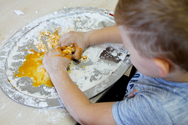 Kilkuletni chłopiec ugniata masę z wody i mąki z dodatkiem przypraw w kolorze żółtym