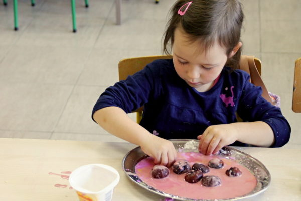 Kilkuletnia dziewczynka macza kasztany w masie plastycznej koloru różowego