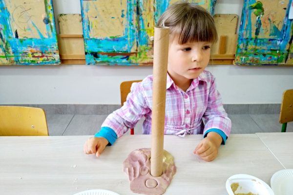 Kilkuletnia dziewczynka i jej praca plastyczna - papierowa tuba wetknięta w masę