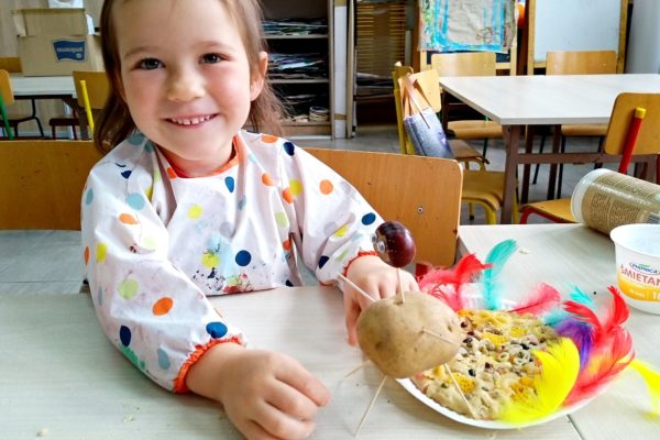 Uśmięchnięta kilkulatka a przed nią praca plastyczna wykonana z masy, ziemniaka i kasztana