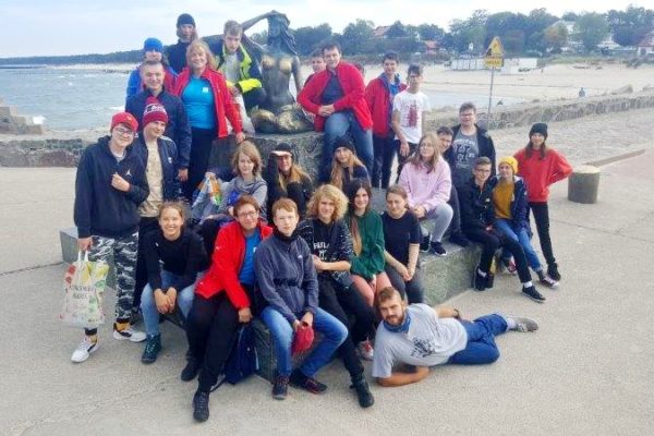 Wspólne zdjęcie uczestników rejsu wraz z opiekunami przy pomniku Usteckiej Syrenki który znajduje się na falochronie. W tle widać fragment morza i plaży