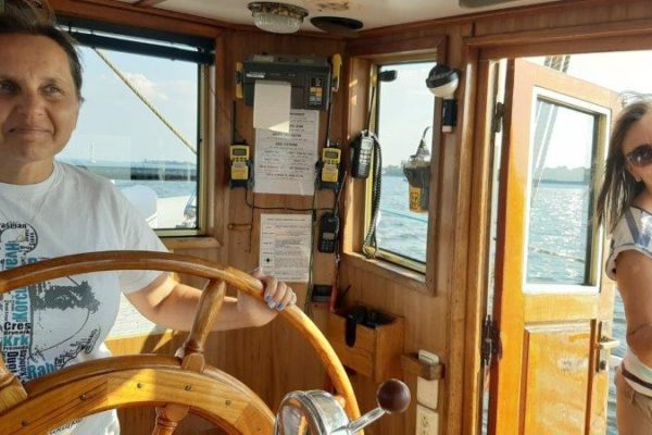 Bożena za kołem steruje żaglowcem, w drzwiach sterówki stoi Wanda
