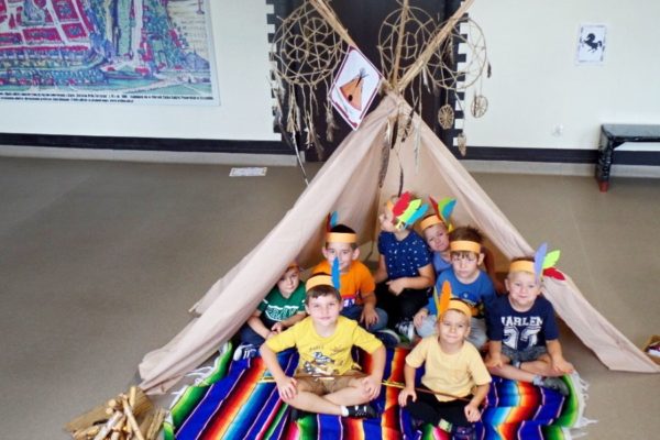grupa przedszkolaków - chłopcy, siedzą w Indiańskim tipi, chłopcy mają na głowie opaski z piórami