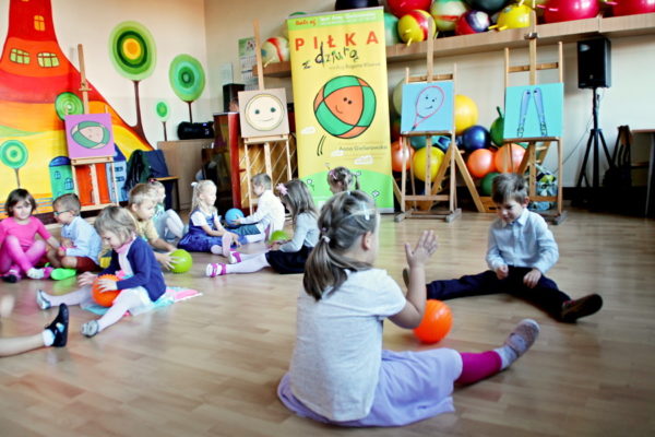 Grupa dzieci siedzących na podłodze, bawią się piłkami