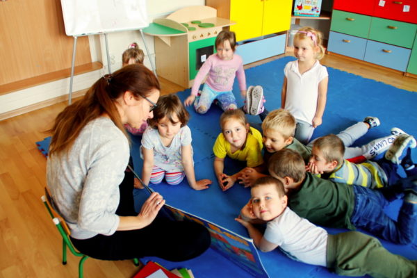 Dzieci skupione wokół nauczycielki czytającej im książkę