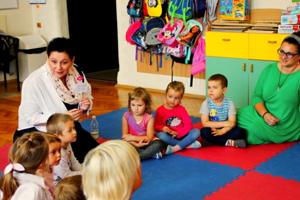 Anna Gielarowska wraz z nauczycielką siedzi na macie z przedszkolakami