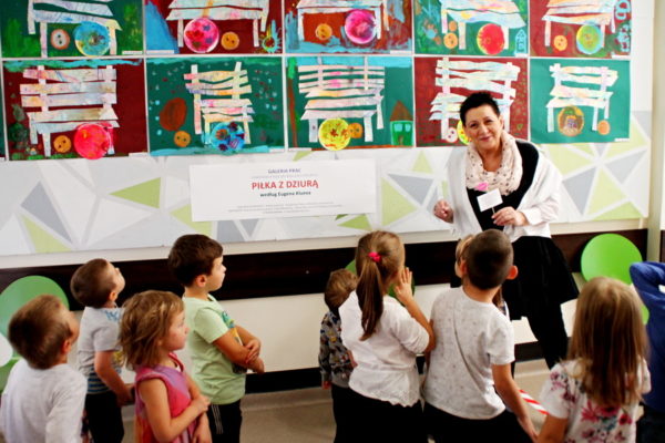 Anna Gielarowska stoi z przedszkolakami przed wystawą ich prac plastycznych
