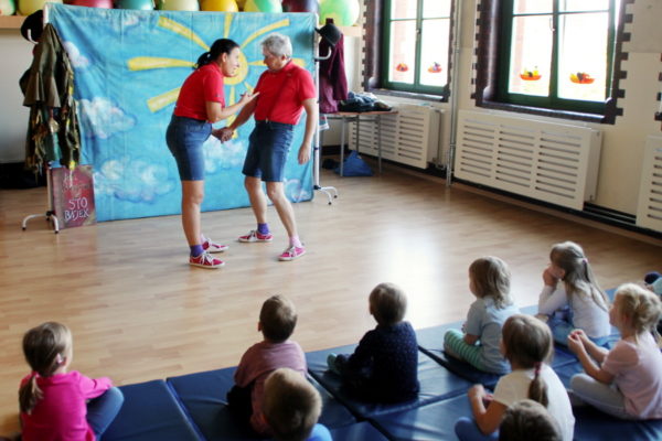 występ aktorów, kobieta i mężczyzna na scenie w sali przedszkolnej, na pierwszym planie dzieci siedzące na macie