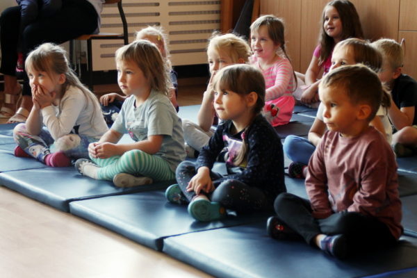 Grupa dzieci - przedszkolaków, siedzą na matach, oglądają przedstawienie