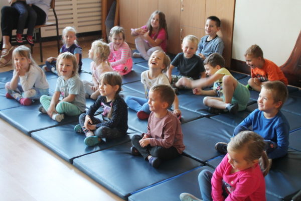 Grupa dzieci - przedszkolaków, siedzą na matach, oglądają przedstawienie, śmieją się