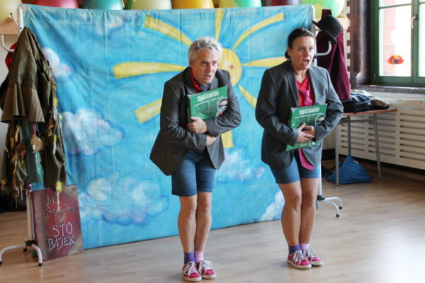 Aktorzy - kobieta i mężczyzna, śpiewają dzieciom, w rękach książka z tytułem "Wędkarstwo"