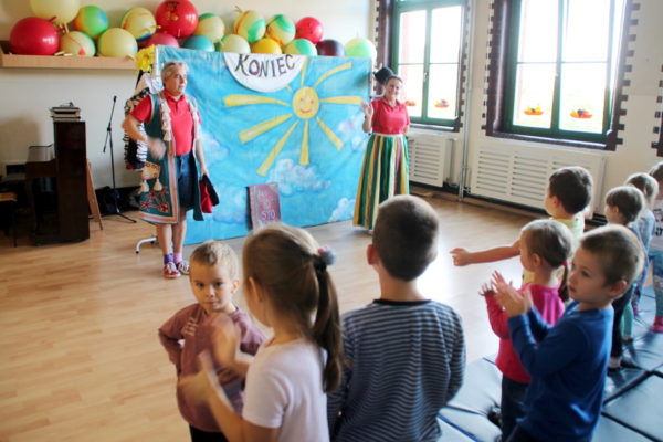Aktorzy Teatru Gwitajcie prezentują się przed dziećmi na scenie w pałacowej sali. Dzieci klaszczą