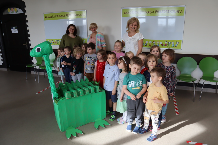 grupa przedszkolaków z nauczycielkami pozuje z kartonowym diznozaurem