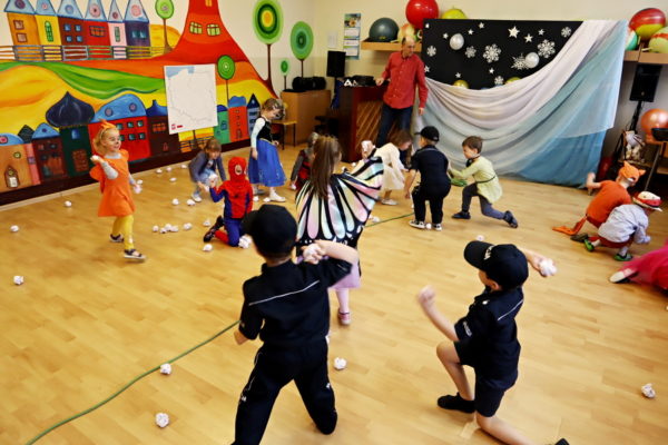 grupa przedszkolaków strojach karnawałowych rzucających kilami papierowymi