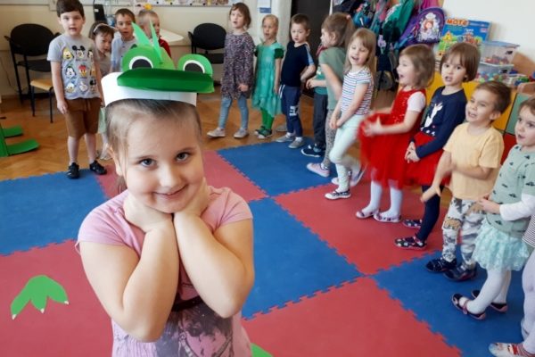 grupa przedszkolaków przy stole na pierwszym planie dziewczynka mająca na głowie czapkę z motywem dinozuara