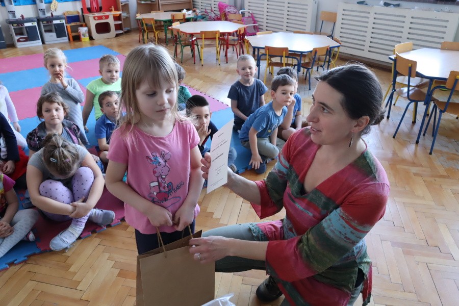 dziewczynka odbiera nagrodę z rąk nauczcielki w tle pozostałe dzieci