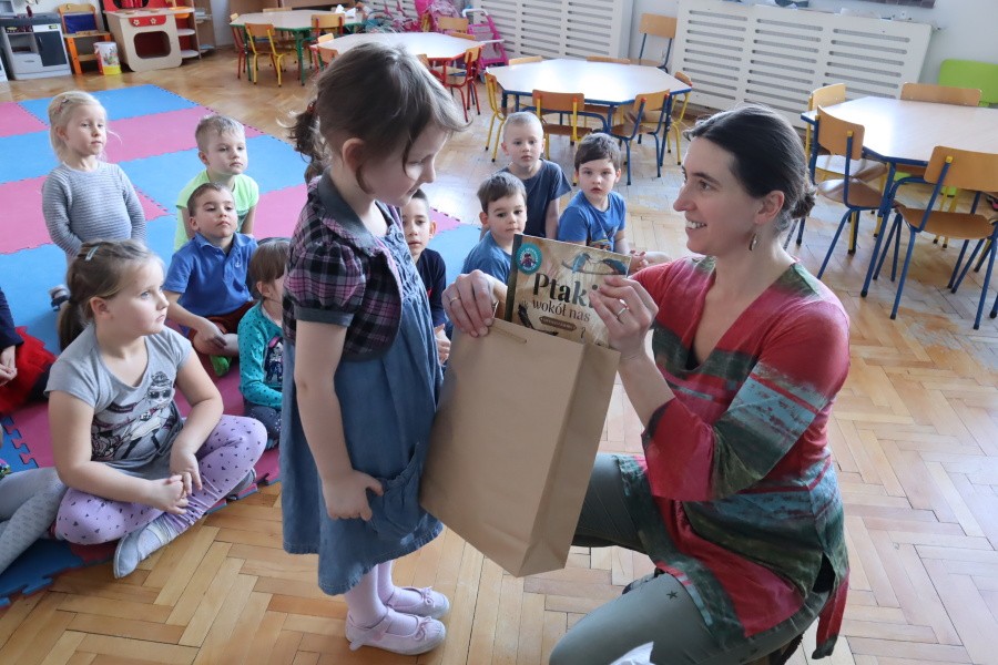 dziewczynka odbiera nagrodę z rąk nauczcielki w tle pozostałe dzieci