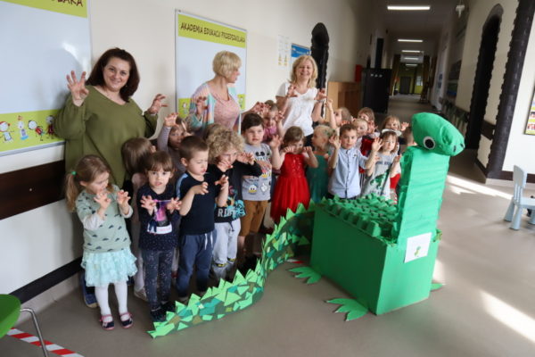grupa przedszkolaków z nauczcielkami i dinozaurem z kartonów