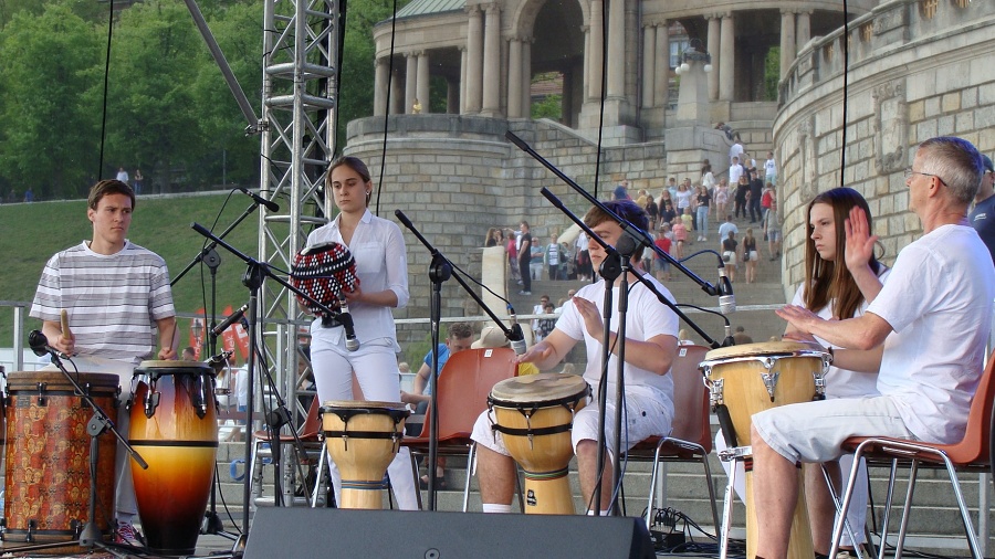 fotografia przedstawia pięcioro ubranych na biało uczniów grających w plenerze na etnicznych instrumentach perkusyjnych.