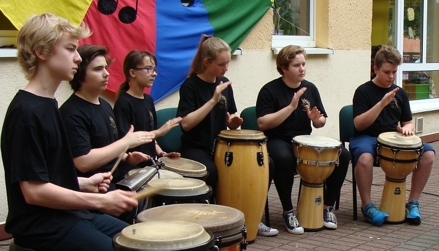 fotografia przedstawia sześcioro uczniów w czarnych strojach grających w plenerze na różnych etnicznych instrumentach perkusyjnych.