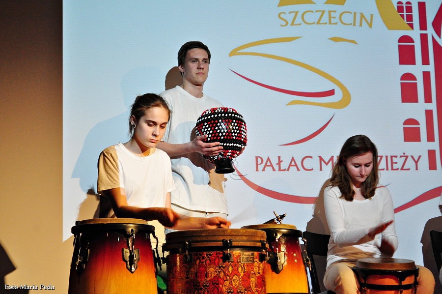 fotografia przedstawia troje uczniów ubranych na biało grających na różnych etnicznych instrumentach perkusyjnych.