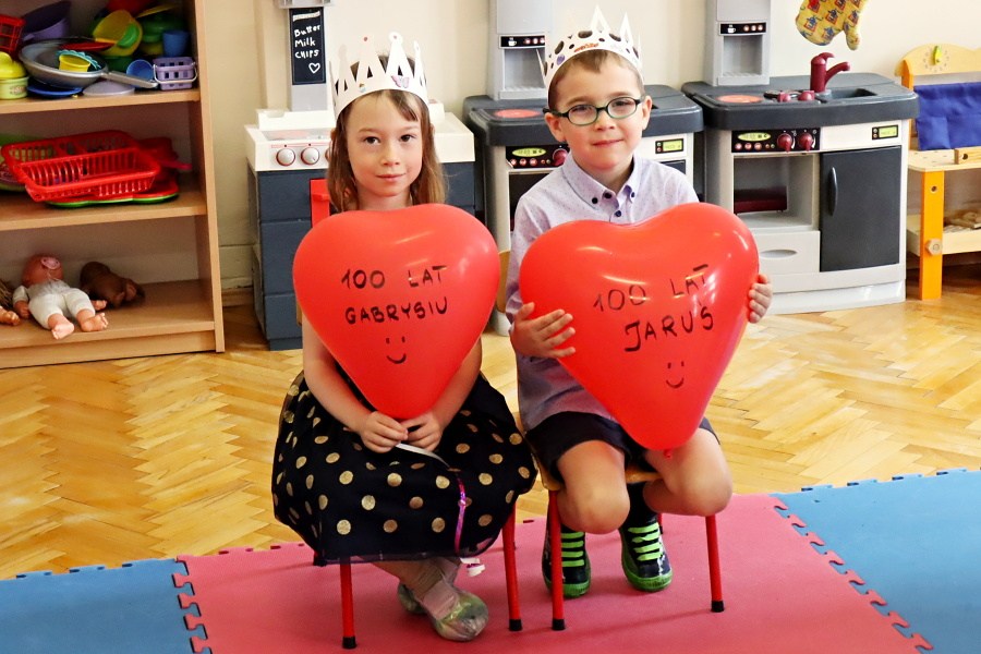 chłopiec i dziewczynka w koroanach na głowei, trzymają balony w kształcie serca