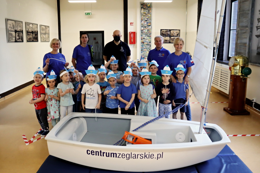 grupa dzieci na pierwszym planie łodka optimist