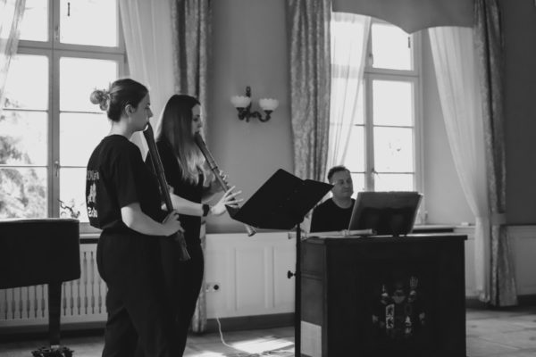 dwie dziewczyny grające na flecie w tle mężczyzna przed instrumentem