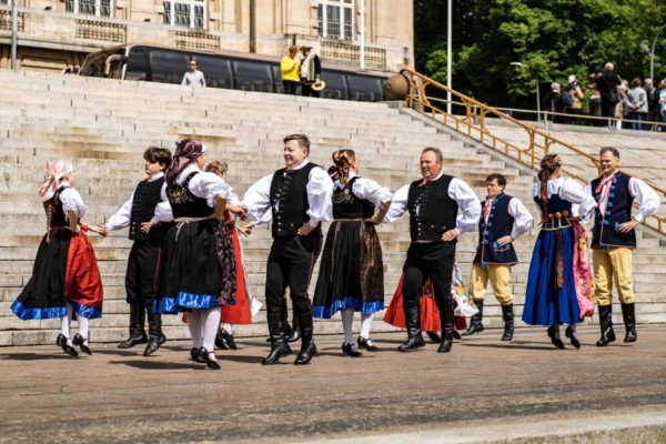 grupa ludzi w strojach ludowych tańczą na tle Wałów Chrobrego