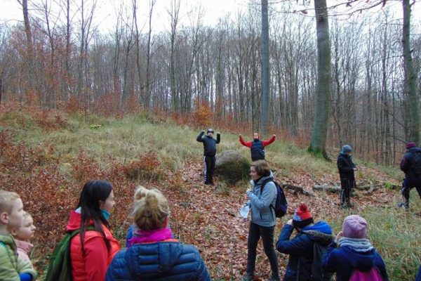 Głaz Błazej, przed nim dwaj chłopcy, inni słuchają ciekawostek o głazie