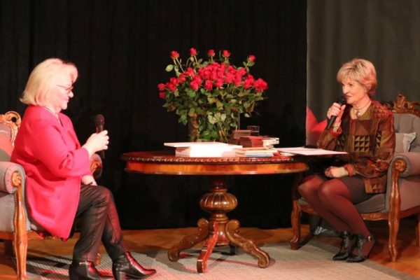 dwie kobiety siedzące przy stoliku rozmawiają z mikrofonami w dłonaich