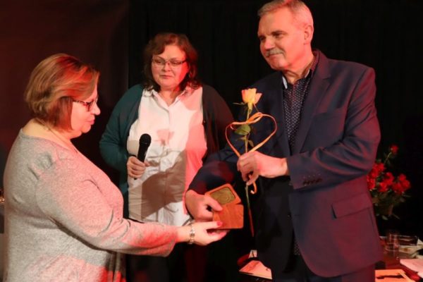 mężczyzna wręcza kobiecie medal i żółtą różę