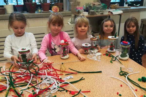 Grupa dziewcząt siedząca przy stole z ozdobami w rękach.