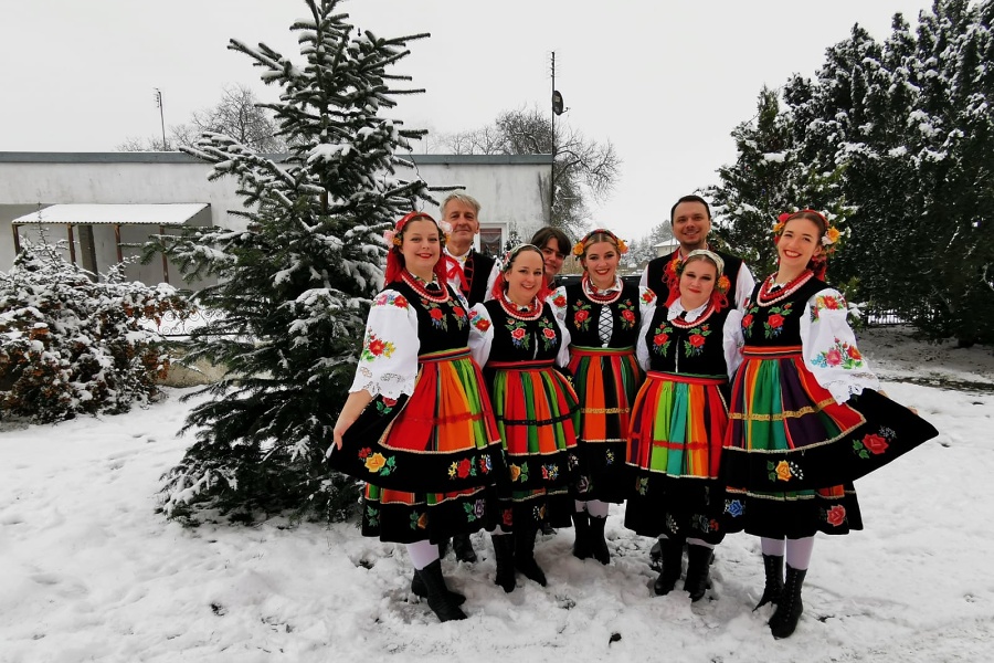 grupa kobiet i mężczyzn w strojach ludowych, pozująca do zdjęcia, w tle zaśnieżone podwórze