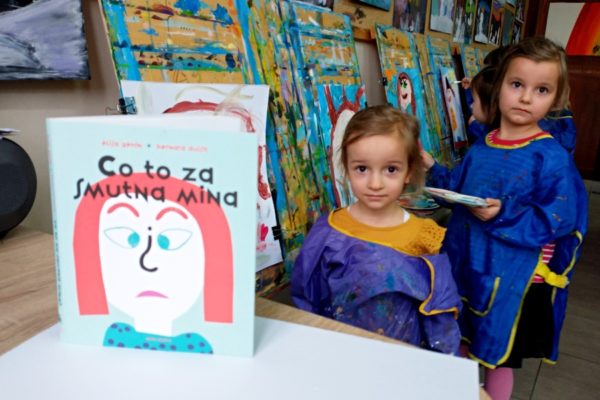 dwie dziewczynki na tle portretów i okładka książki