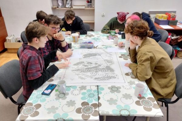 uczestnicy pracowni pochyleni nad stołem, rysują