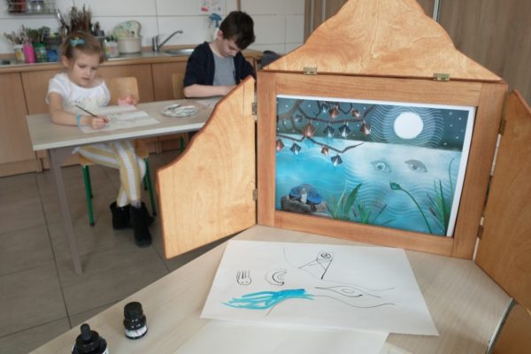 na pierwszym tel teatrzyk kamishibai w tle dzieci malujące