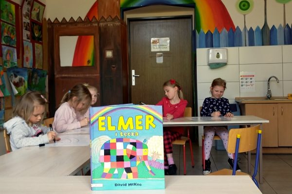 uczestnicy pracowni plastycnzej podcza malowania na pierwszym planie okładka ksiażki o Elmerze