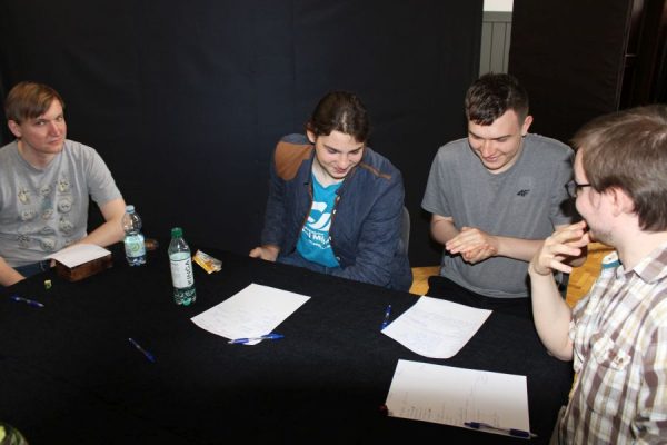 grupa młodzieży siedząca przy stole i grające w gry RPG