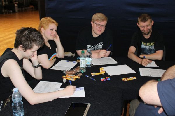 grupa młodzieży siedząca przy stole i grające w gry RPG