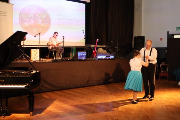 na piewrwszym planie para taneczna w układzie na scenie młody człowiek z instrumentem