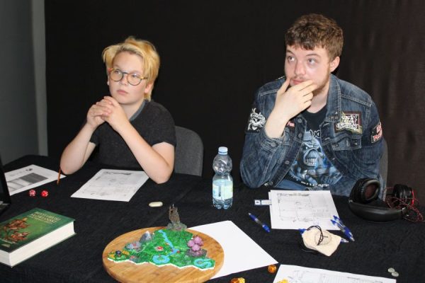 grupa młodzieży siedząca przy stole i grające w gry RPG