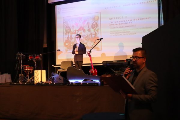 mężczyzna z mikrofoenem, w tle na scenie czeka artysta