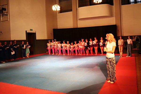 grupa tancerek stoi za przemawiajacą przez mikrofon wicedyrektor Pałacu