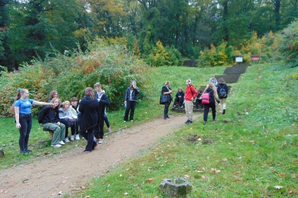 rupa młodzieży odpoczywa na polanie, w tle schody kamienne i las