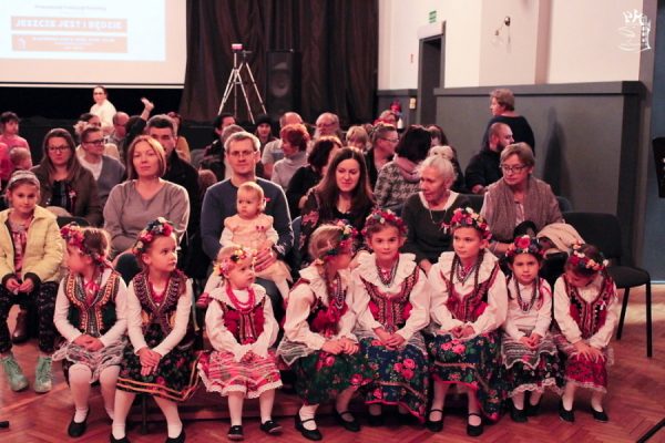 grupa tancerzy w strojach ludowych, za nimi publiczność