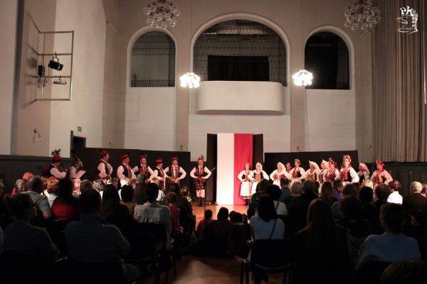 grupa tancerzy w strojach ludowych na pierwszym planie publiczność