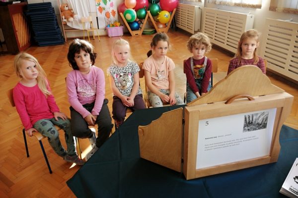 dzieci siedzą przed nimi teatrzyk kamishibai